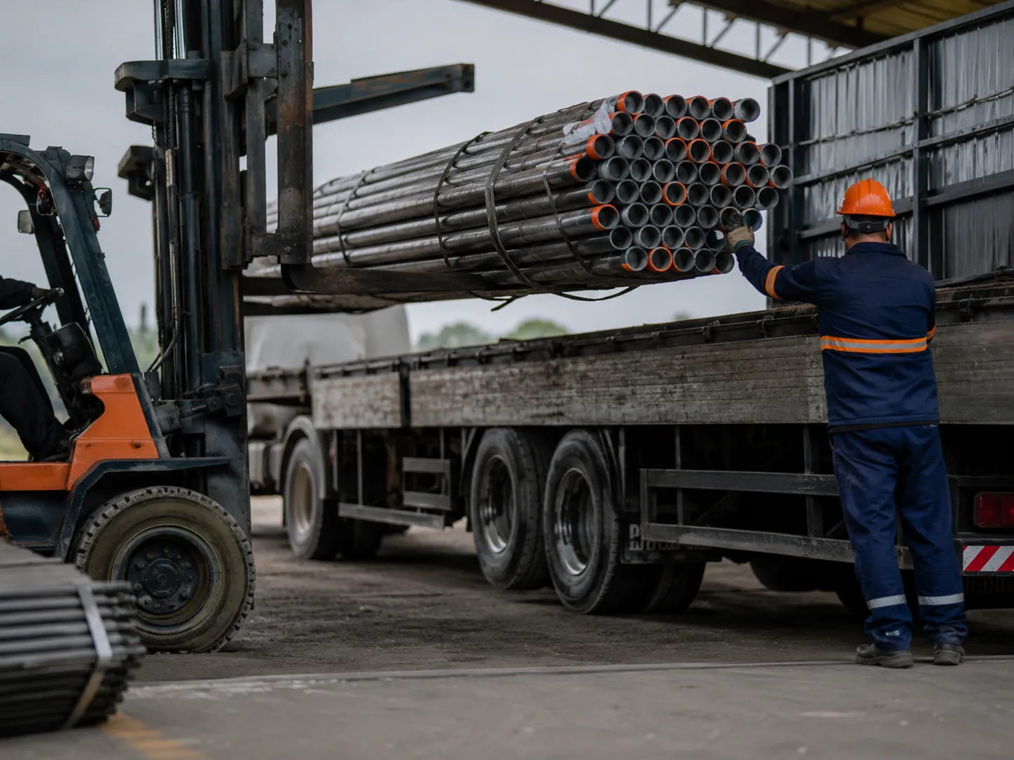 Empilhadeira carregando tubos de aço em um caminhão no pátio da distribuidora